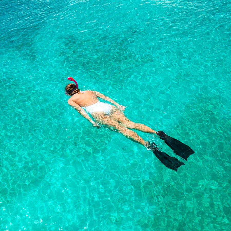 Woman snorkeling in white bathing suit against turquoise waters. 