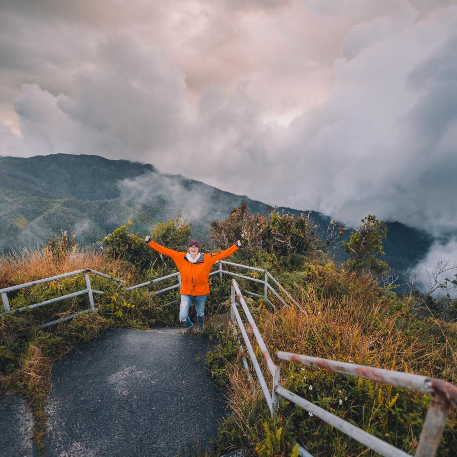 A woman raises her arms triumphantly after hiking up the side of a mountain.