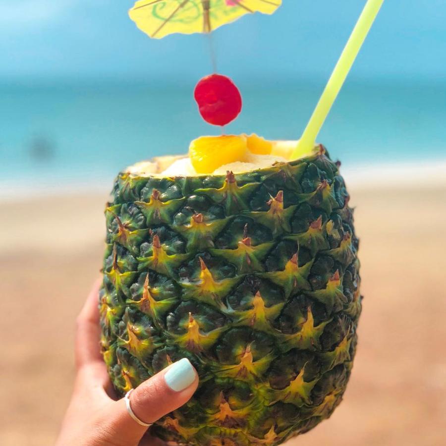 A hand holding a pineapple filled with piña colada.