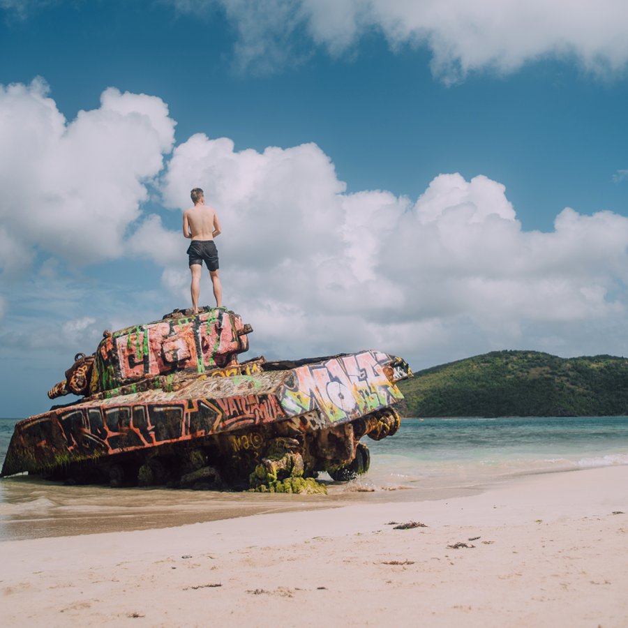 A man stands at the top of an abandoned war tank in Flamenco Beach