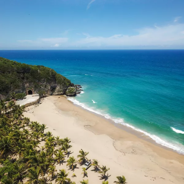An aerial view of the Tunel de Guajataca adjacent to a white sand beach and turquoise sea.