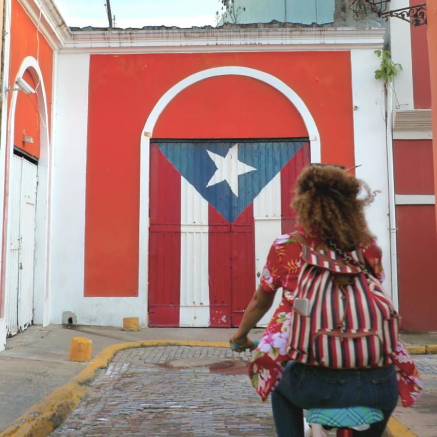 Waoman riding a bike in front of Puerto Rican flag mural on cobblestoned street