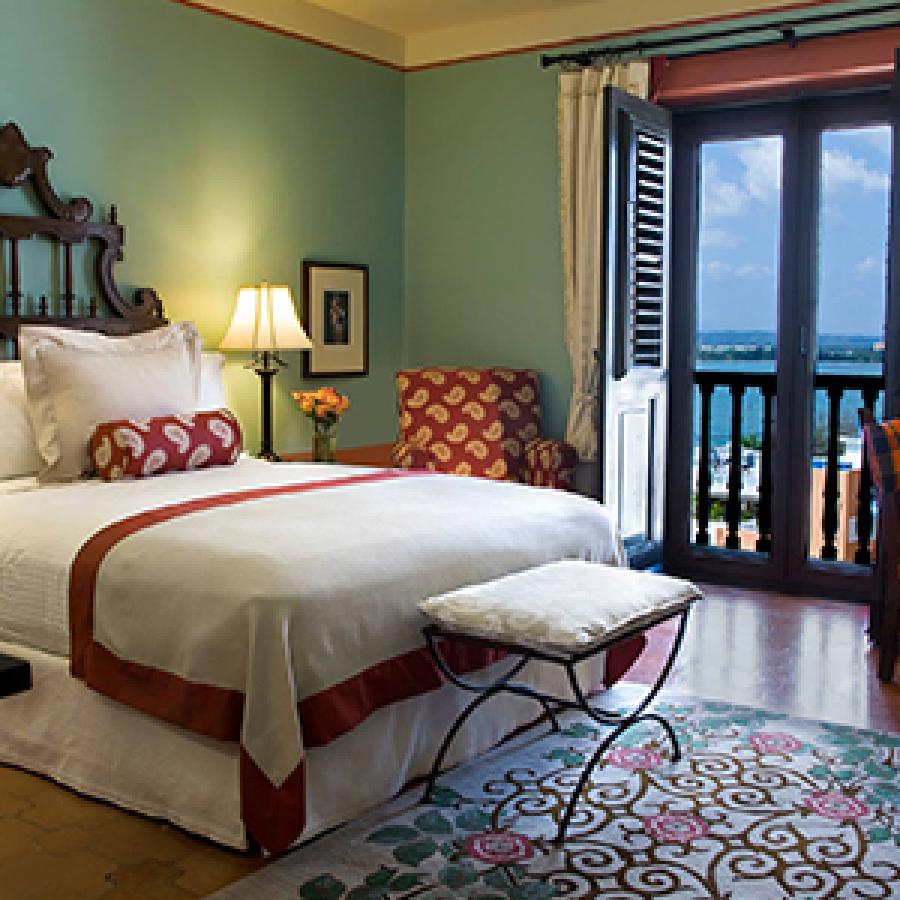 Photo of interior of hotel room with one large bed and windows opening up to an ocean view.