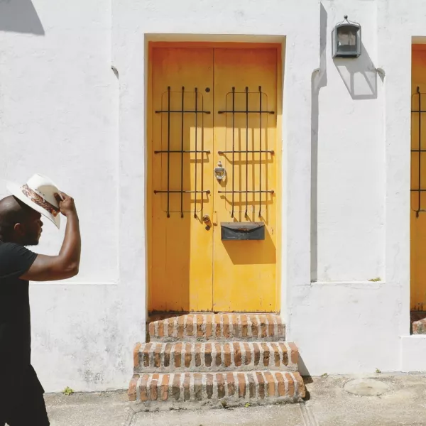 Man walking down a sunny street in front of yellow doorways