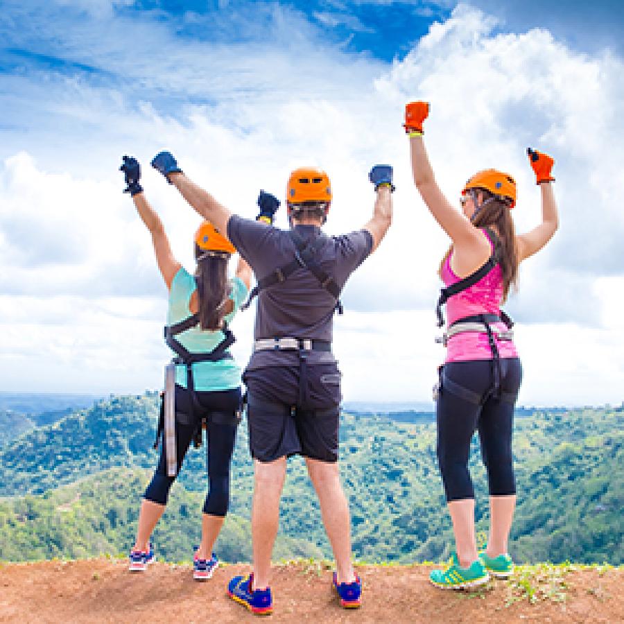 Three people with hands in the air wearing zipline gear.