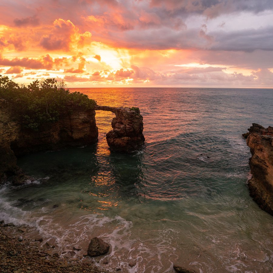 A dramatic sunset over the ocean with a beach surrounded by rock formations in the foreground