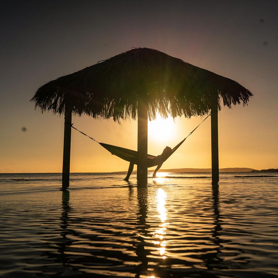 A person relaxes in a hammock as the sun sets in the background
