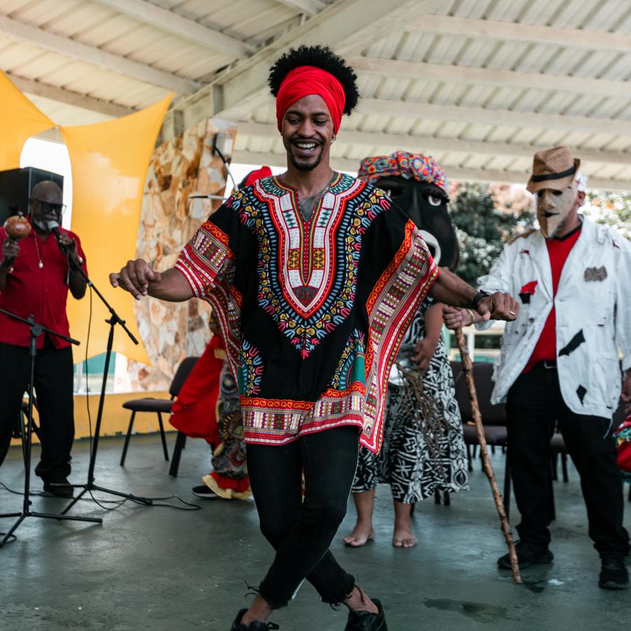 El hombre afrocaribeño baila al son de la música bomba, mientras que otros bailarines y músicos están en el fondo.