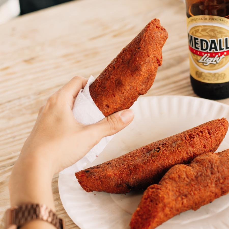 Person holds a Puerto Rican fritters known as alcapurria with a local beer in the background.