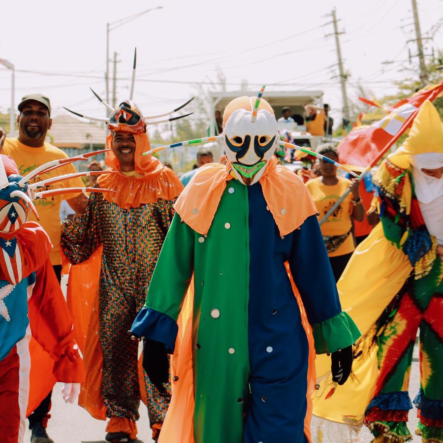 A colorful group of people dressed in the tradional attire of Puerto Rican vejigantes, which includes colorful masks. 
