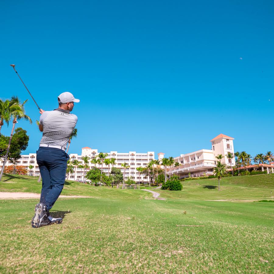 Man swings is golf club in a lush golf course with views of El Conquistador Hotel.