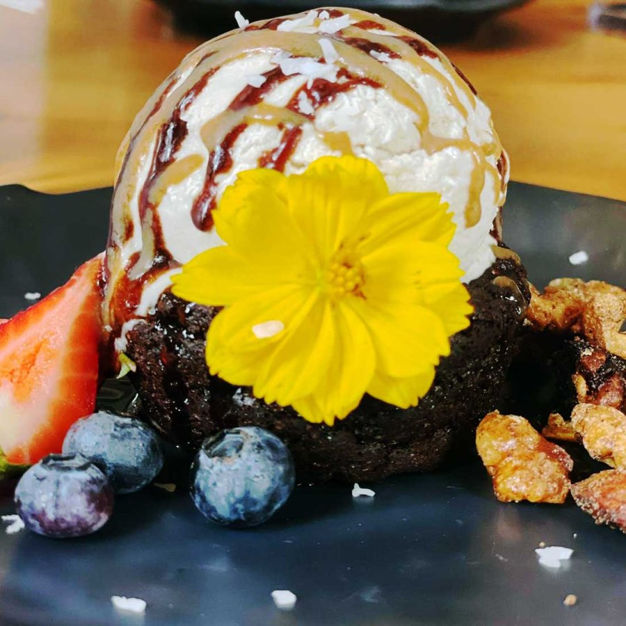 A vegan chocolate brownie topped with vegan vanilla ice cream and decorated with edible flowers and fruit.