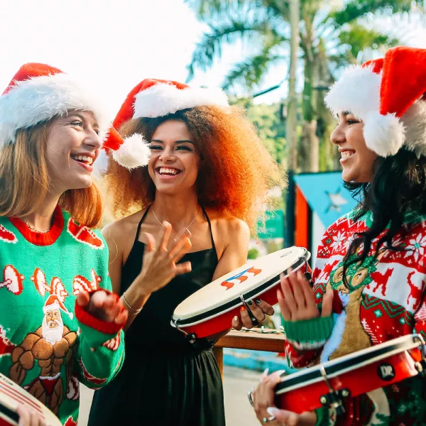 Three young ladies wearing Santa hats and Christmas sweaters playing the pandero, a typical instrument of Puerto Rico's Christmas parrandas.
