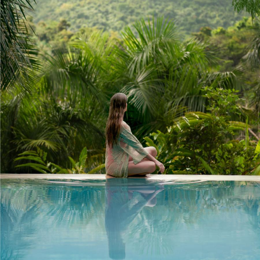 A woman gazes out over a mountainous forest from a pool in Rio Grande, Puerto Rico