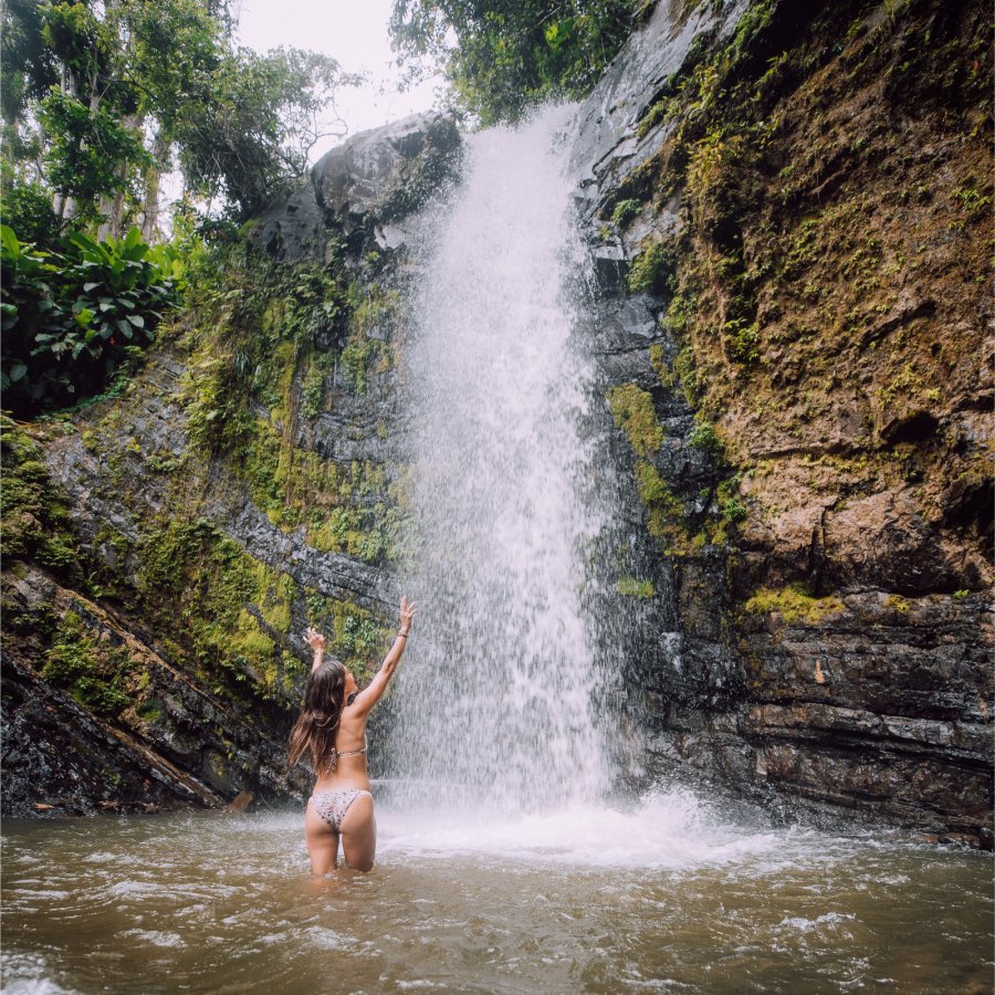 A woman frolics in a waterfall pool at Juan Diego Falls in El Yunque National Forest