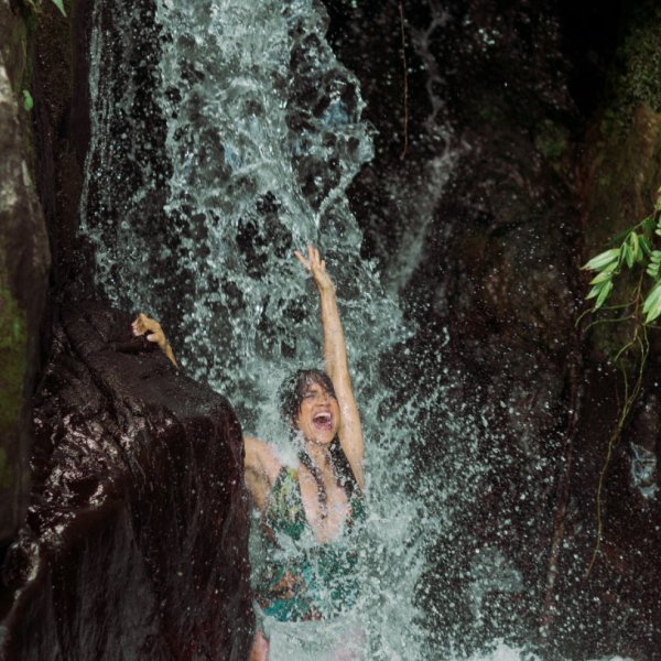A woman enjoys playing under a waterfall, one of the fun things to do in Puerto Rico for adventure seekers.