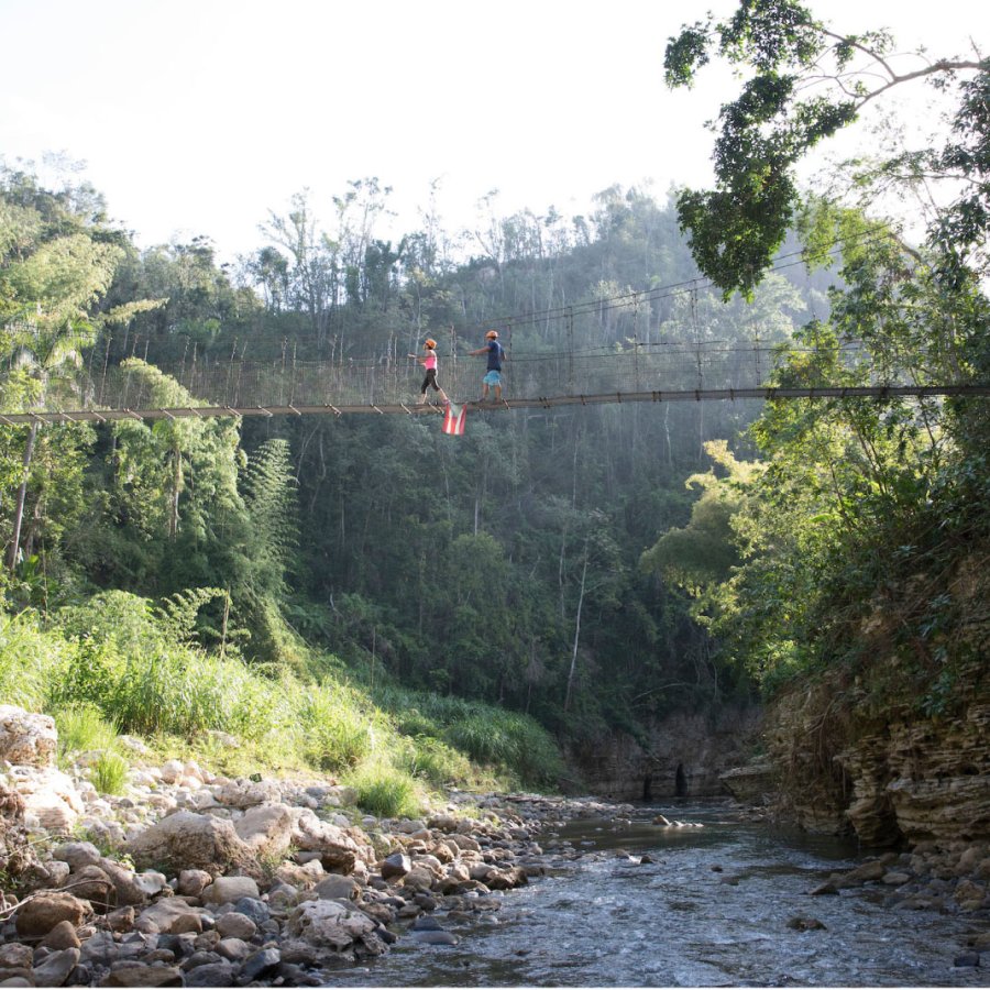 A pair of travelers walk over a bridge on the Tanama River in Utuado, Puerto Rico.