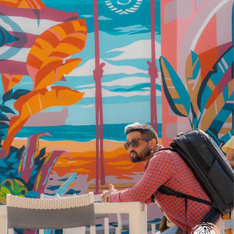Muralist Angelo Alvarez sits at an outdoor table in front of a brightly colored mural in Puerto Rico.