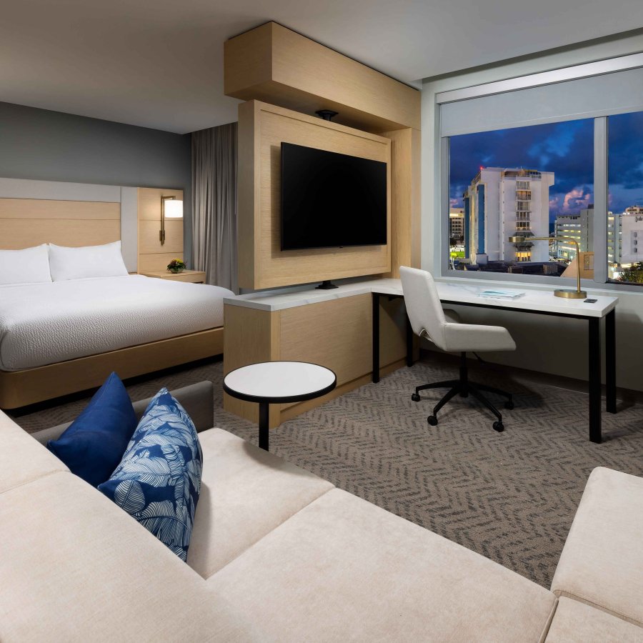 Interior of a large king suite room at the Residence Inn by Marriott San Juan Isla Verde, with a large window overlooking a city scene at night.