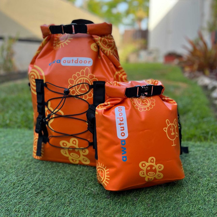 Two dry bags in the bright orange shade of Puerto Rico Sunshine sit on display atop green grass.
