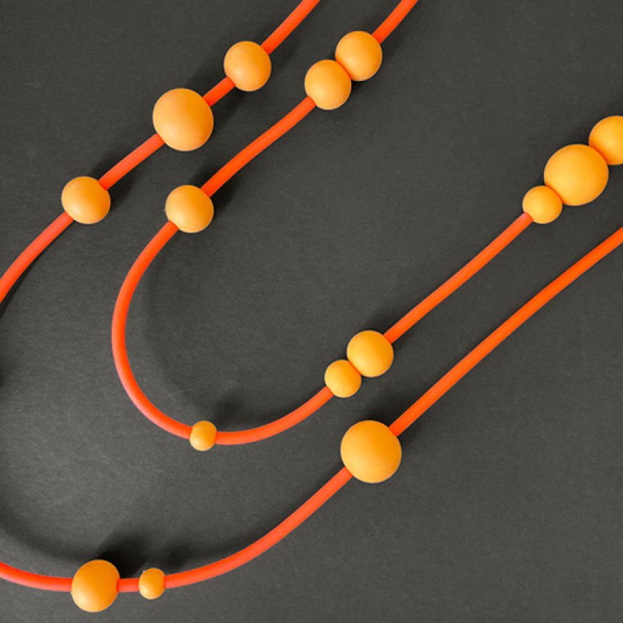 Overhead shot of a beaded necklace by Knot Predictable in shades of orange on a black background.