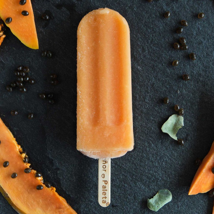 An orange popsicle is pictured on a black background surrounded by orange fruit slices.