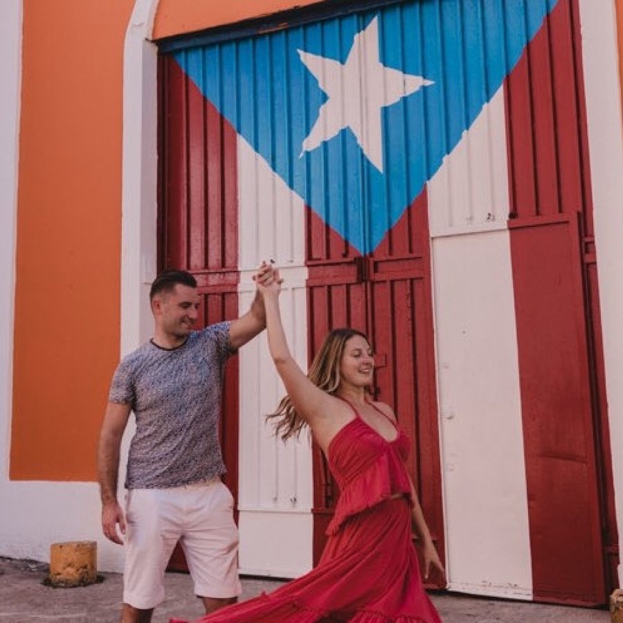 A couple poses in front of a door with the Puerto Rican Flag