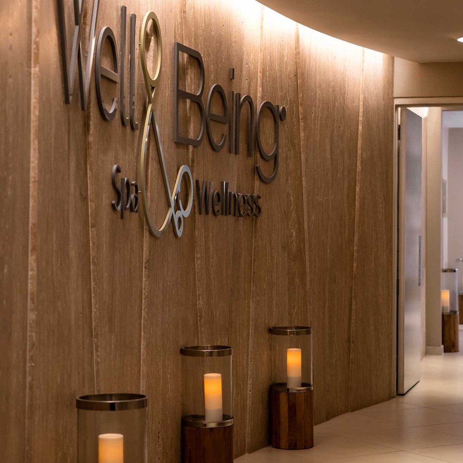 A man in a spa robe walks down a long hallway in front of a wooden wall with the words "Well & Being." 