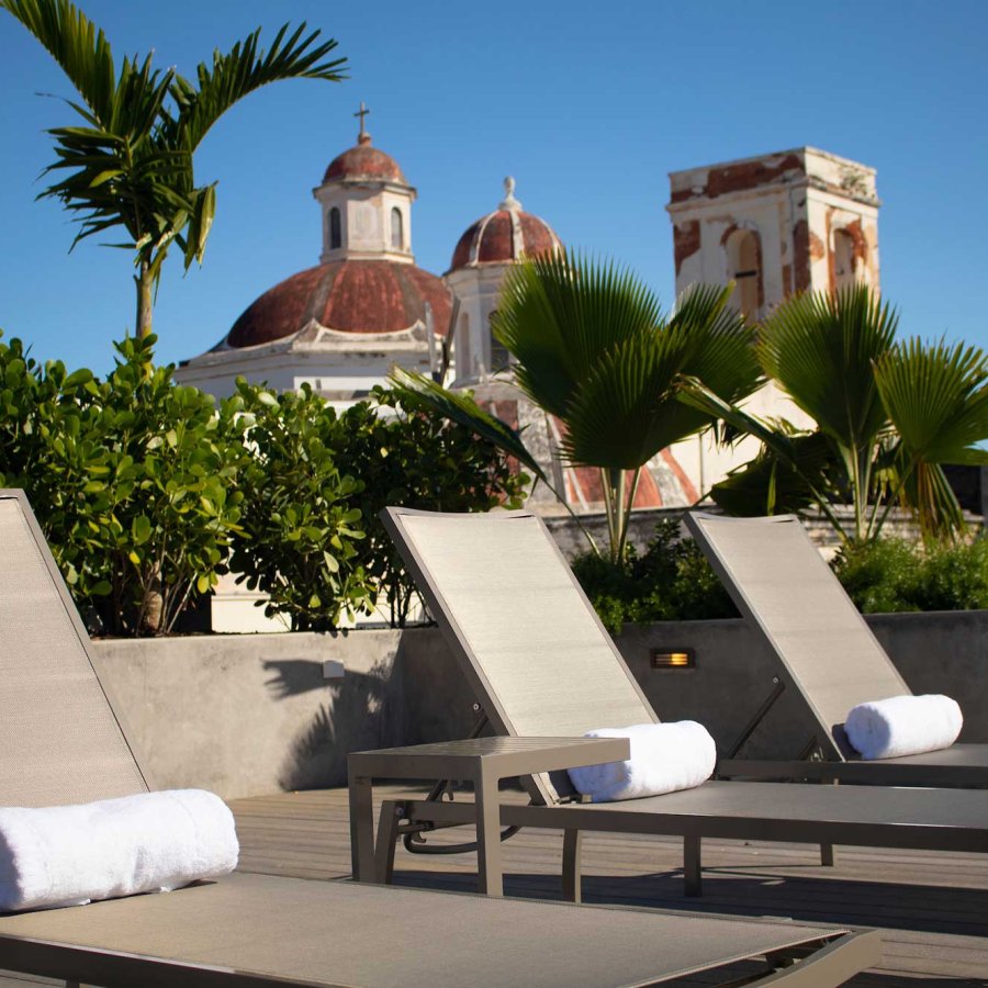 A row of lounge chairs with rolled up pool towels, with a historic rooftop of Old San Juan rising up in the background.