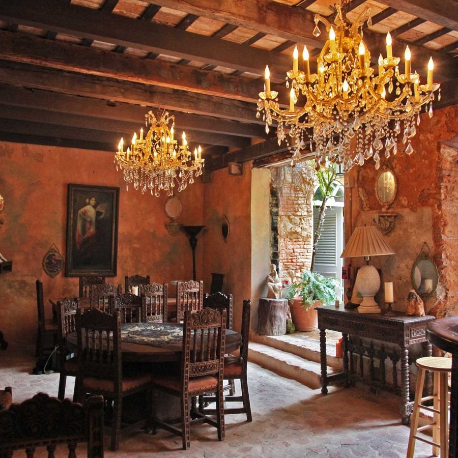 A common space at the Gallery Inn in San Juan, Puerto Rico, features a large antique chandelier, ceilings with exposed wood beams, and large doorways into a lush courtyard.