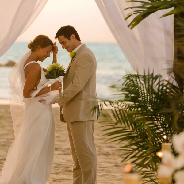 A bride and groom face each other in front of an altar draped with white fabric on a beach in Puerto Rico.