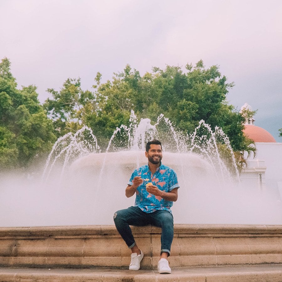 Man enjoying his ice cream while sitting on the ledge of a large fountain in downtown Ponce.