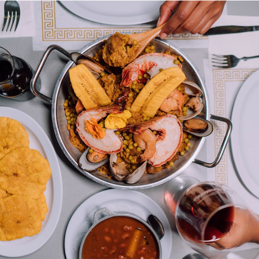 A plate of savory seafood paella served alongside tostones and red wine at El Balcon de Capitan in Salinas.