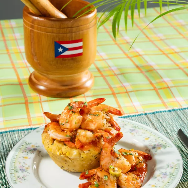 Plate of traditional Puerto Rican mofongo served with crispy pork and a wooden mortar in the background.