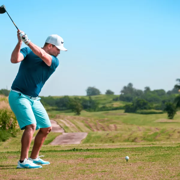 Golfer mid-swing on the fairways of Royal Isabela Golf Course in Puerto Rico, with lush green hills and palm trees in the background.