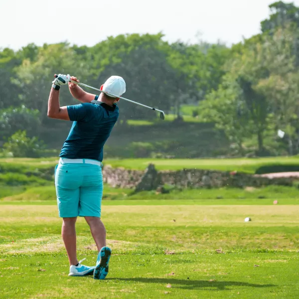 A golfer finishes a powerful swing on a lush green golf course of Royal Isabela..