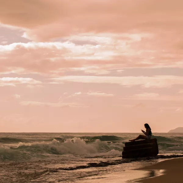 A person sitting on a rock at Tres Palmas Marine Reserve in Rincón, Puerto Rico, during sunset with waves rolling in.