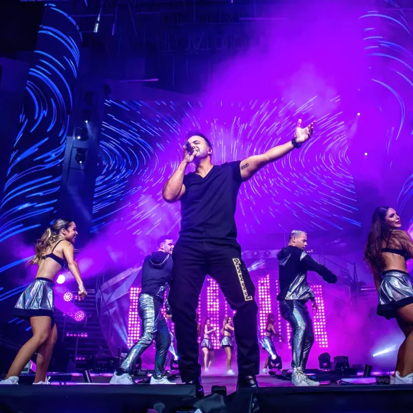 Singer performing on a brightly stage with dancers and colorful lights.