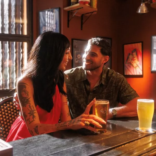 Couple sitting at a cozy bar in Puerto Rico, smiling at each other while enjoying cold beers in a warmly lit indoor setting.