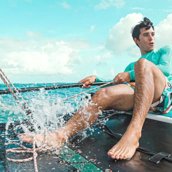 Man sailing a small catamaran in turquoise waters off Puerto Rico, pulling ropes as waves splash across the deck under a bright blue sky.