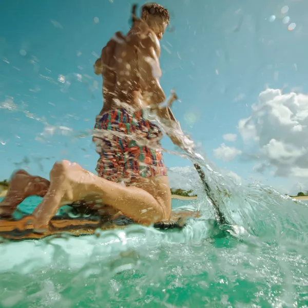 Man paddleboarding through clear turquoise water on Puerto Rico’s east coast, splashing waves near a tropical shoreline under a bright blue sky.