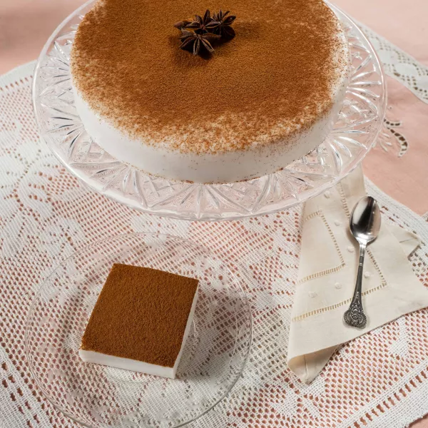 Tembleque coconut dessert topped with cinnamon, served on a glass stand with a sliced piece on a plate.