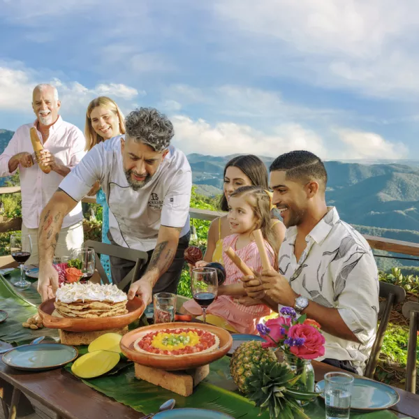 Chef serves a colorful puerto rican dish to a group at a scenic outdoor table, surrounded by mountains and greenery from Cayey, Puerto Rico.