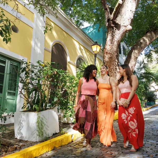 Three women walking on a cobblestone street in Old San Juan wearing colorful outfits from Valija.