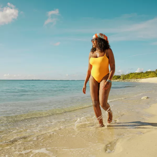 Woman walking along a beach wearing a yellow swimsuit and a colorful headscarf