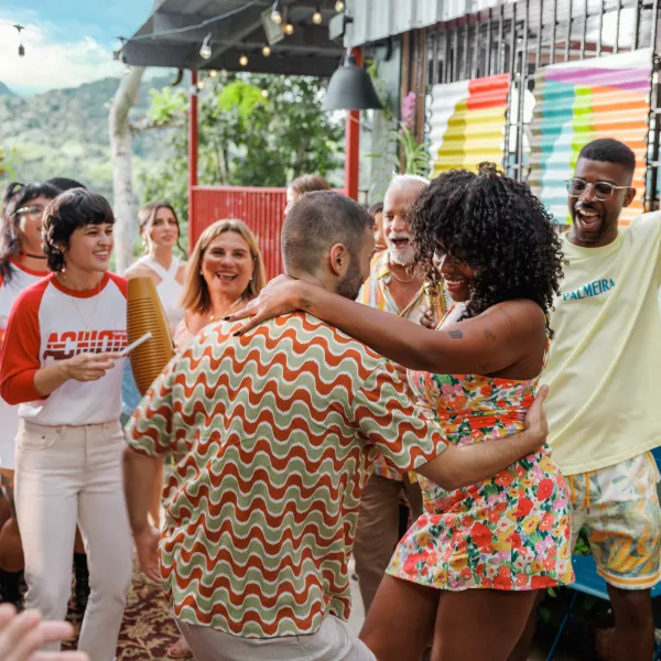 Una mujer radiante con un vestido floral baila en una fiesta al aire libre en Cayey, Puerto Rico, acompañada por una tocadora de güiro tradicional, decoración colorida y vistas a las montañas.