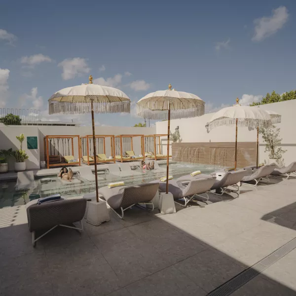 Outdoor pool at Bali Posh Hotel with cushioned lounge chairs, shaded cabanas, and fringed umbrellas under a sunny blue sky