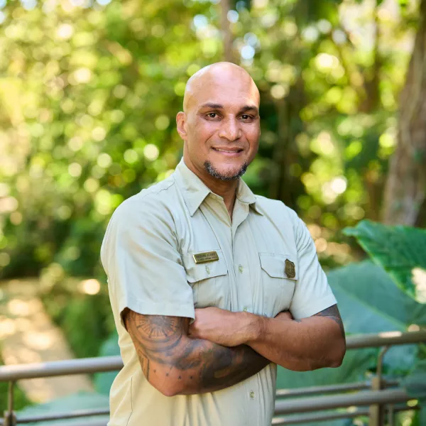 Dr. Keenan Adams, forest supervisor, standing with arms crossed on a trail in El Yunque rainforest, surrounded by lush green vegetation.
