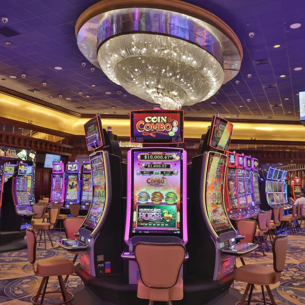 The interior of Foxwoods El San Juan Casino featuring rows of modern slot machines with colorful digital displays under a grand, ornate crystal chandelier and a blue coffered ceiling.