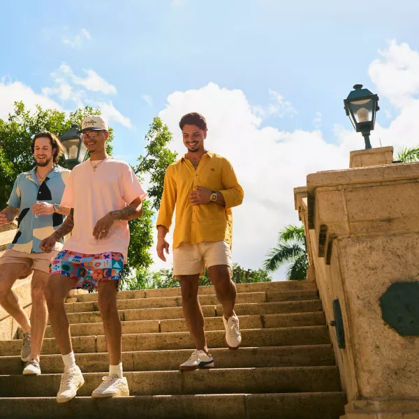 Three men wearing relaxed, colorful clothing walking down stone steps under a bright sky in Old San Juan